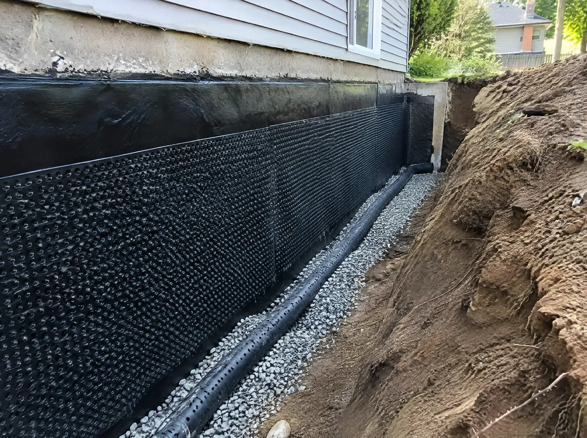 Excavated foundation wall sealed with membrane and drainage board, new weeping tile at the footing